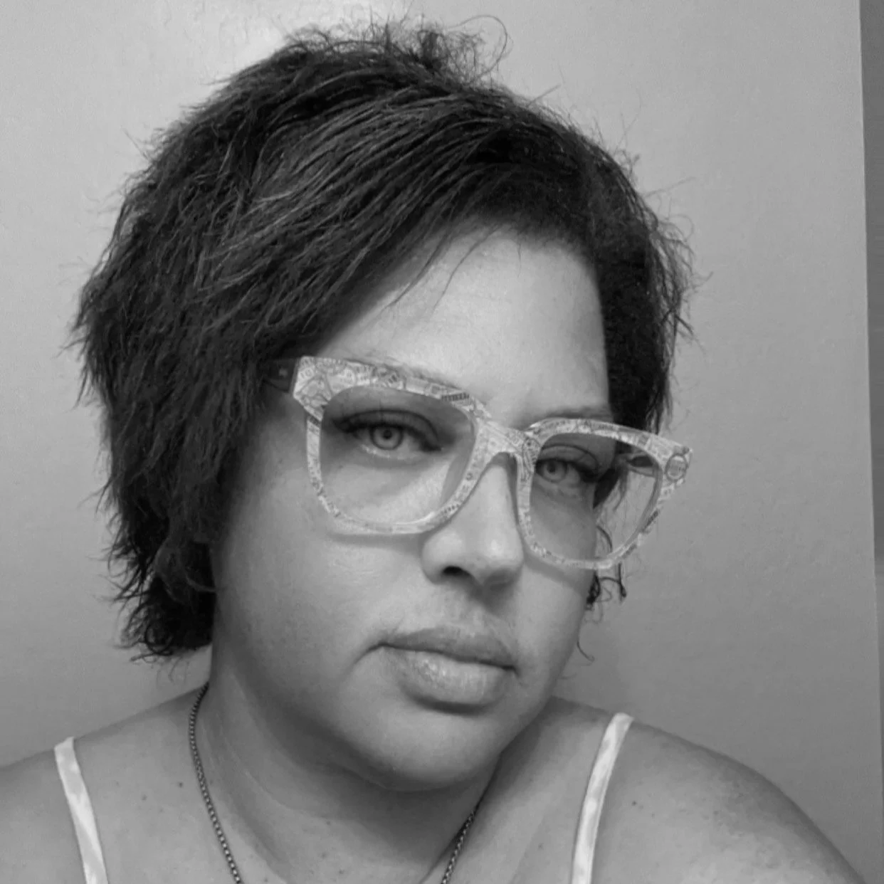 Black and white close-up photo of a woman wearing patterned glasses, with short dark hair, looking directly at the camera.