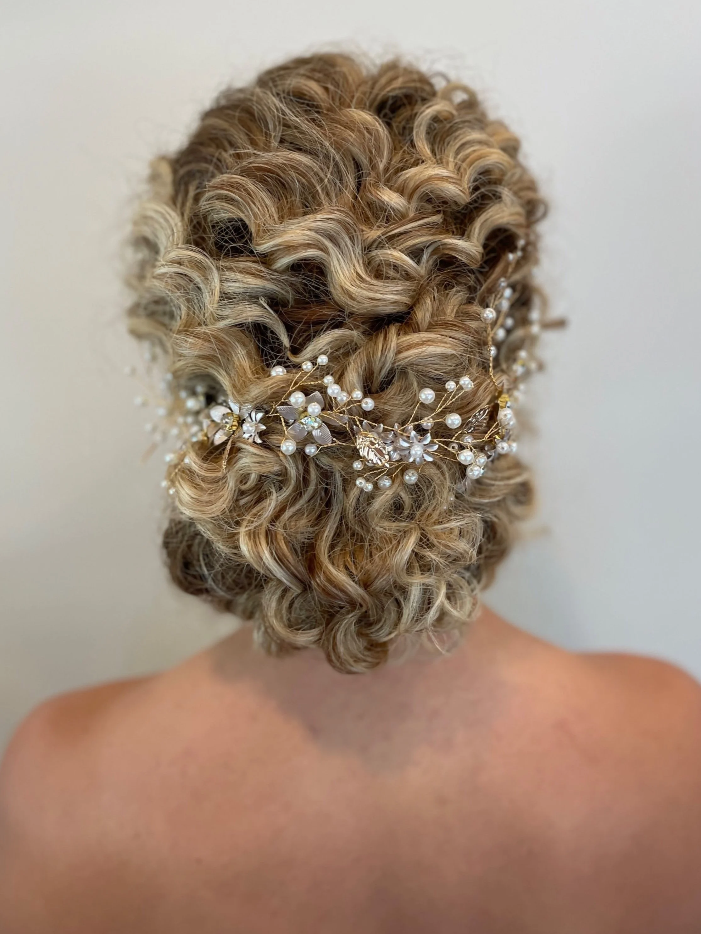 Romantic low bun for curly hair adorned with pearl and gold hair accessory by Maryland bridal stylist