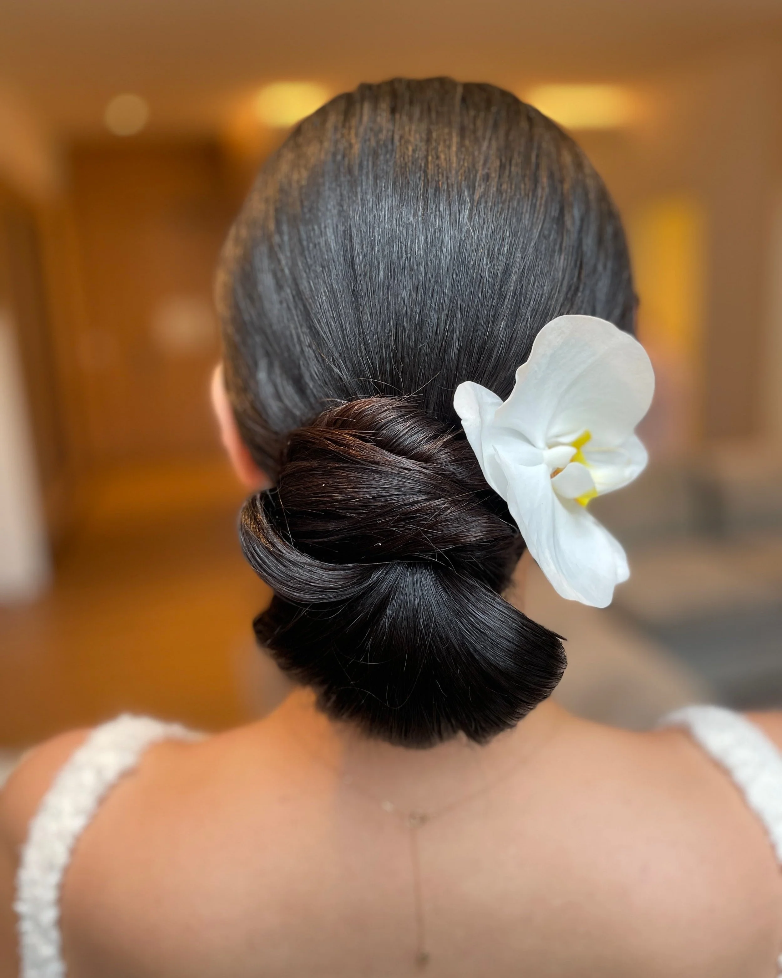 Classic chignon , adorned with a white flower, styled by Frederick Maryland bridal beauty artist.