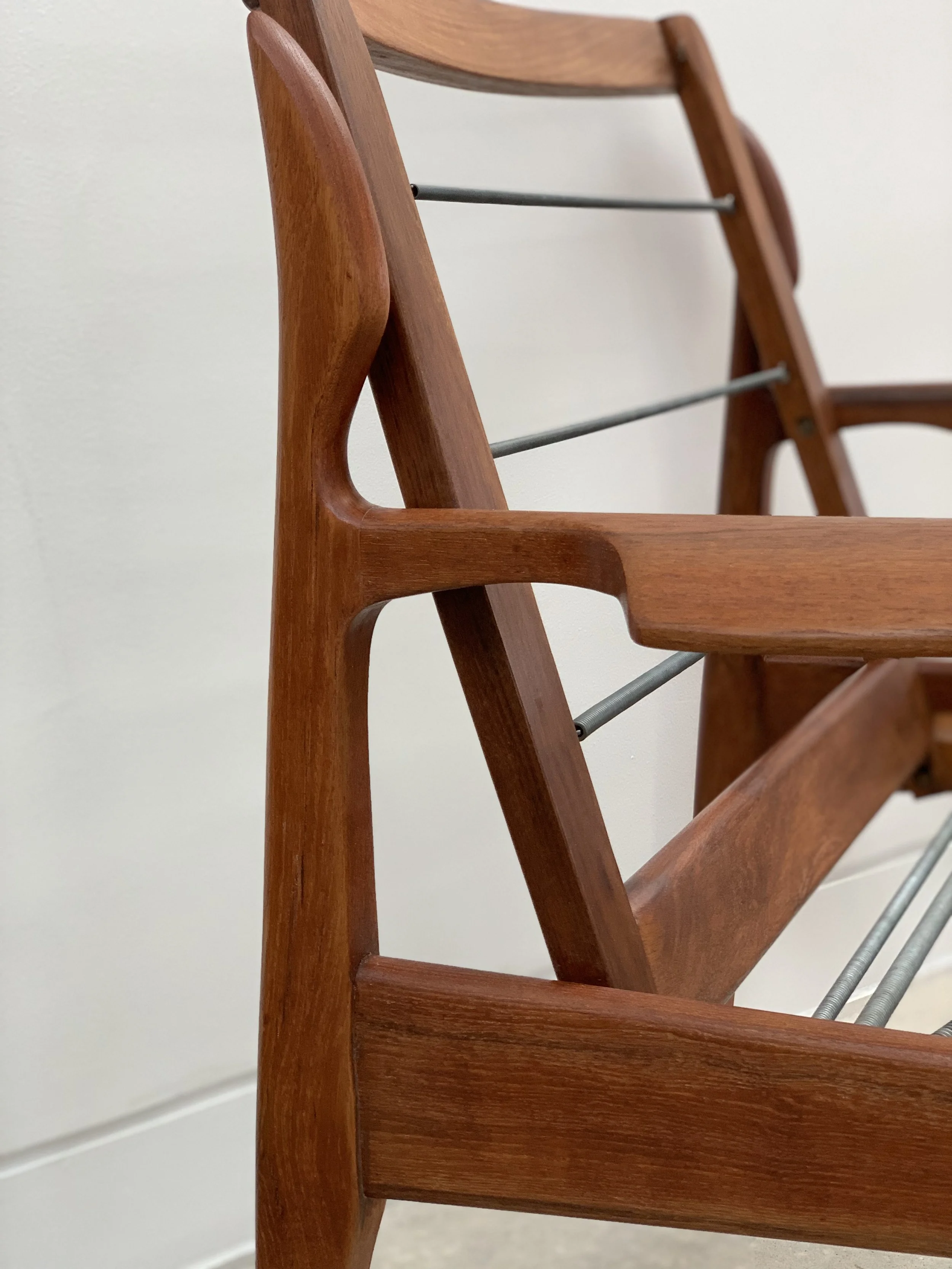 Close-up of the corner of a wooden chair with metal support rods, against a plain off-white wall.