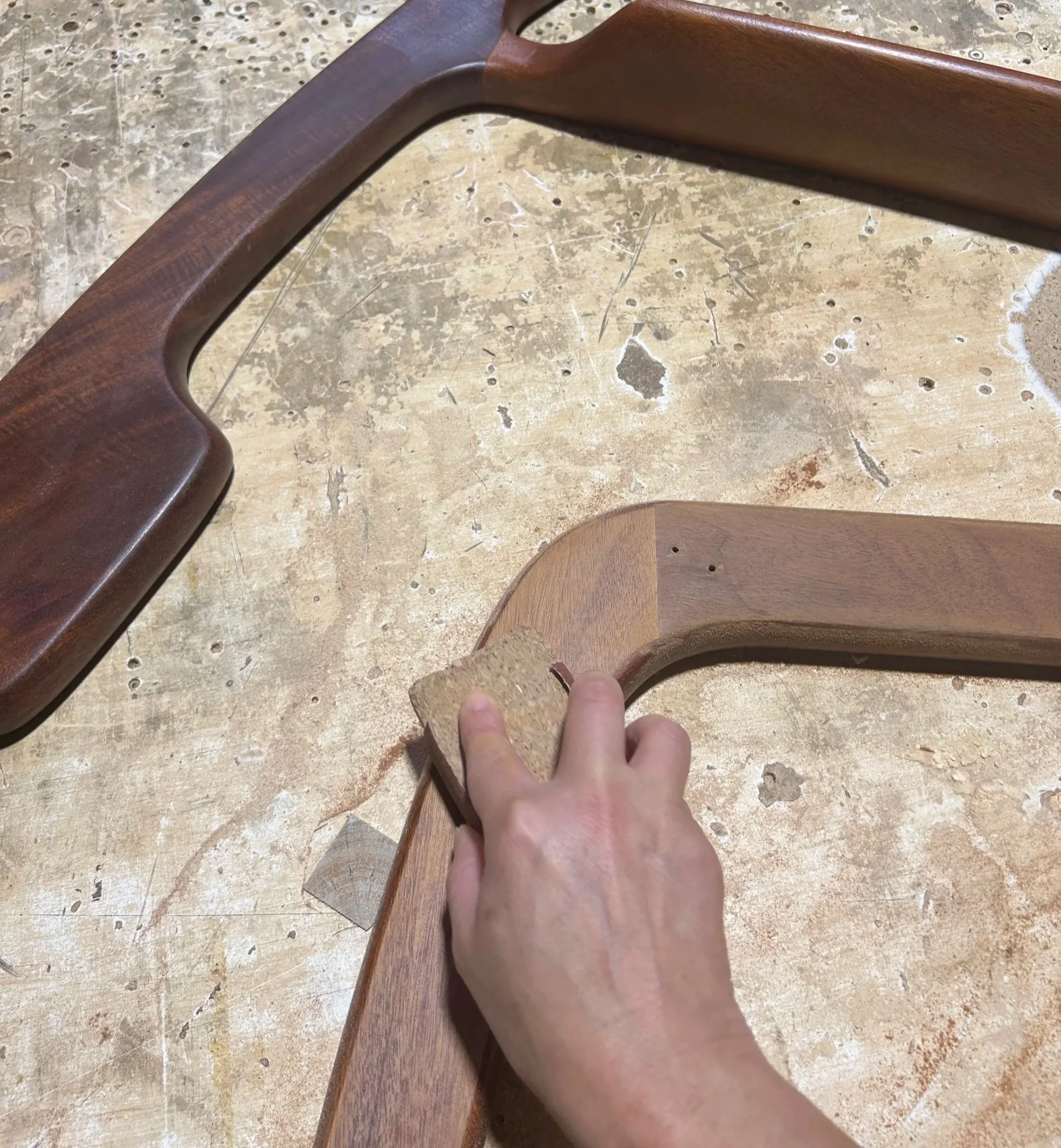 a female hand sanding an arm of a chair against a bench