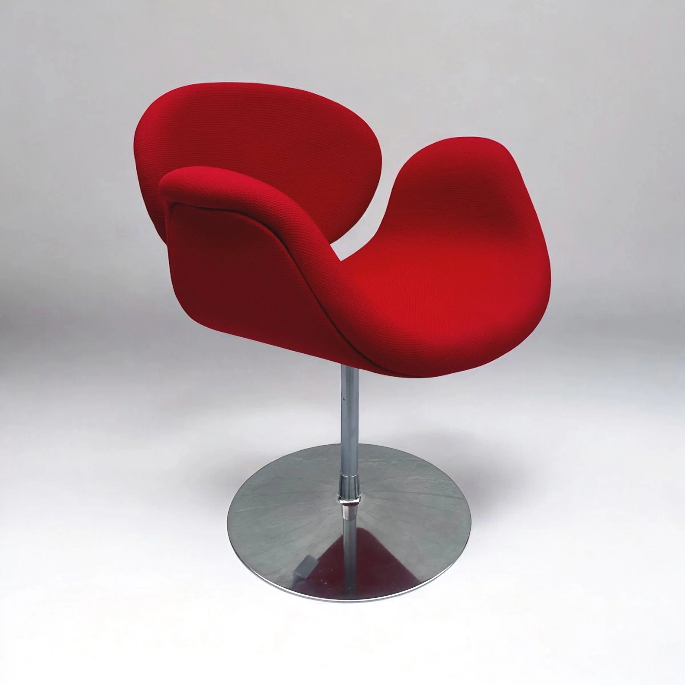 A modern red chair with a curved backrest and matching seat, mounted on a silver pedestal base, set against a plain white background.