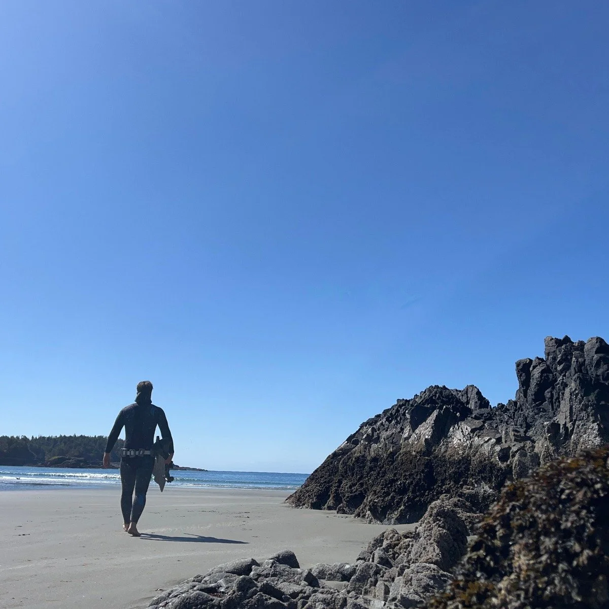  A man walking towards an ocean on a sand beach with large volcanic rock formations next to him. 