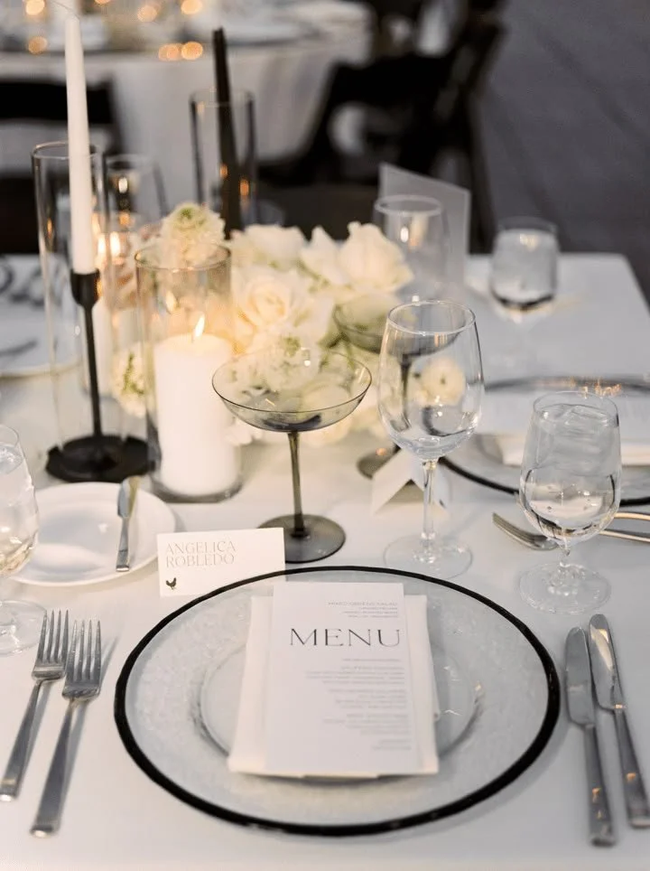 Elegant table setting with white floral centerpiece, candles, wine glasses, and a menu card at a formal event.