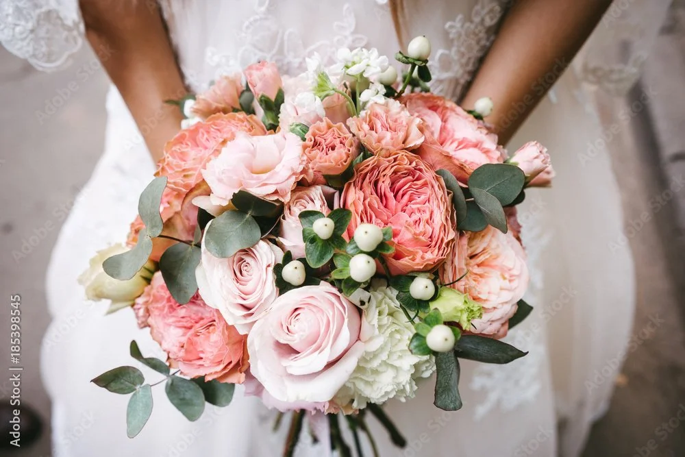 A bride holding a bouquet of pink and white roses, hydrangeas, eucalyptus, and berries.