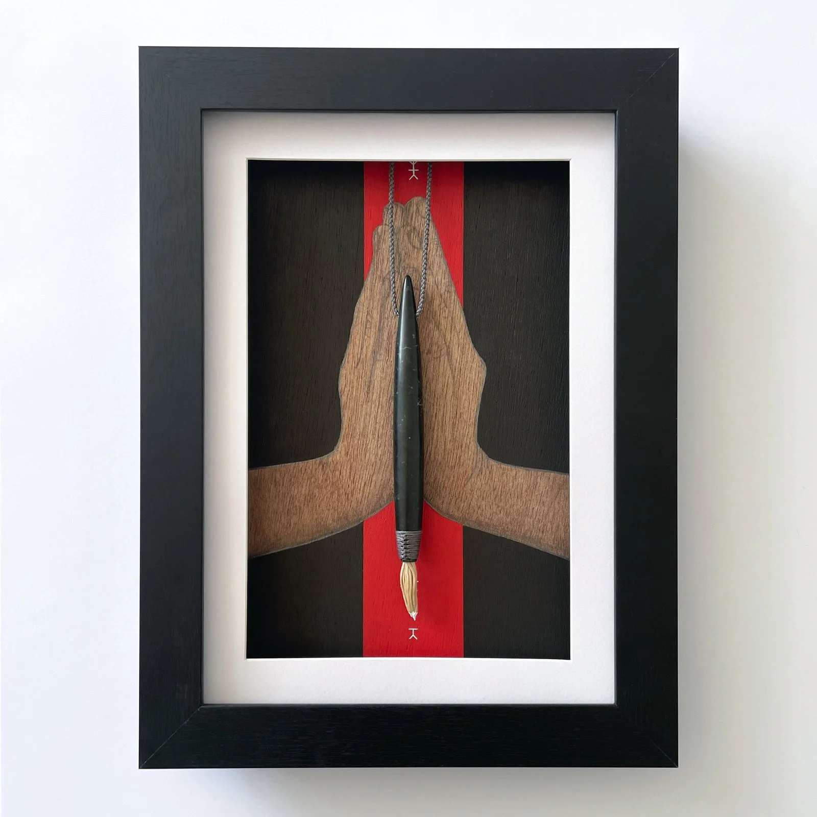 Pounamu carved paintbrush in front of a painting in frame.