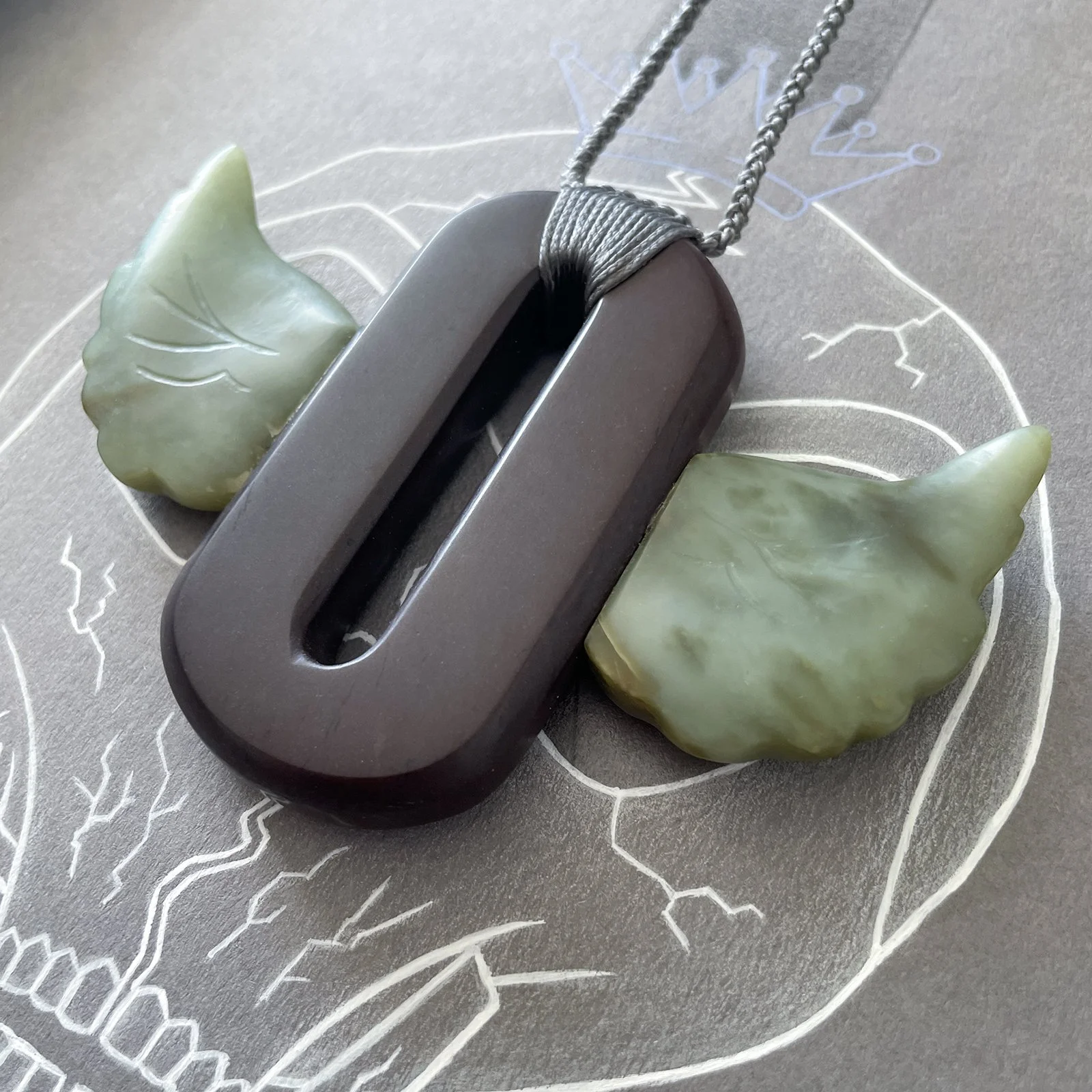 Close-up of stone carved necklace of the Outkast “winged-O” symbol, made from Purple Jasper and Inanga Pounamu.