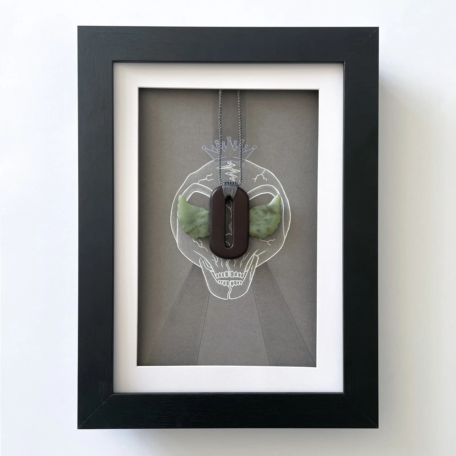 Outkast framed artwork with a stone carved necklace of their “winged-O” symbol displayed in front of a mixed media piece (graphite, acrylic paint and gloss varnish) of 2 'ATLien' skull halves meeting. Two seperate paths become one in the eye sockets 