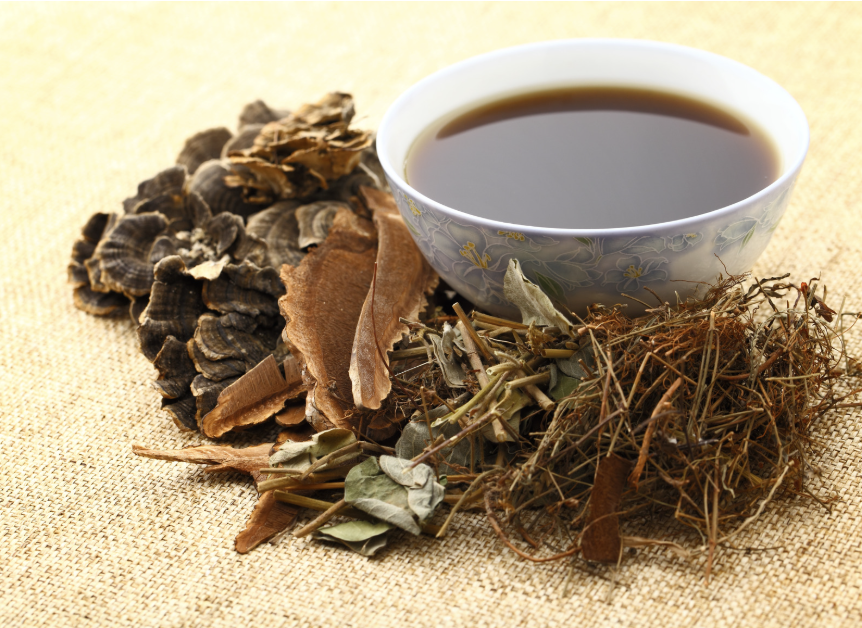 Traditional Chinese medicine herbs with a cup of herbal tea on a burlap surface.