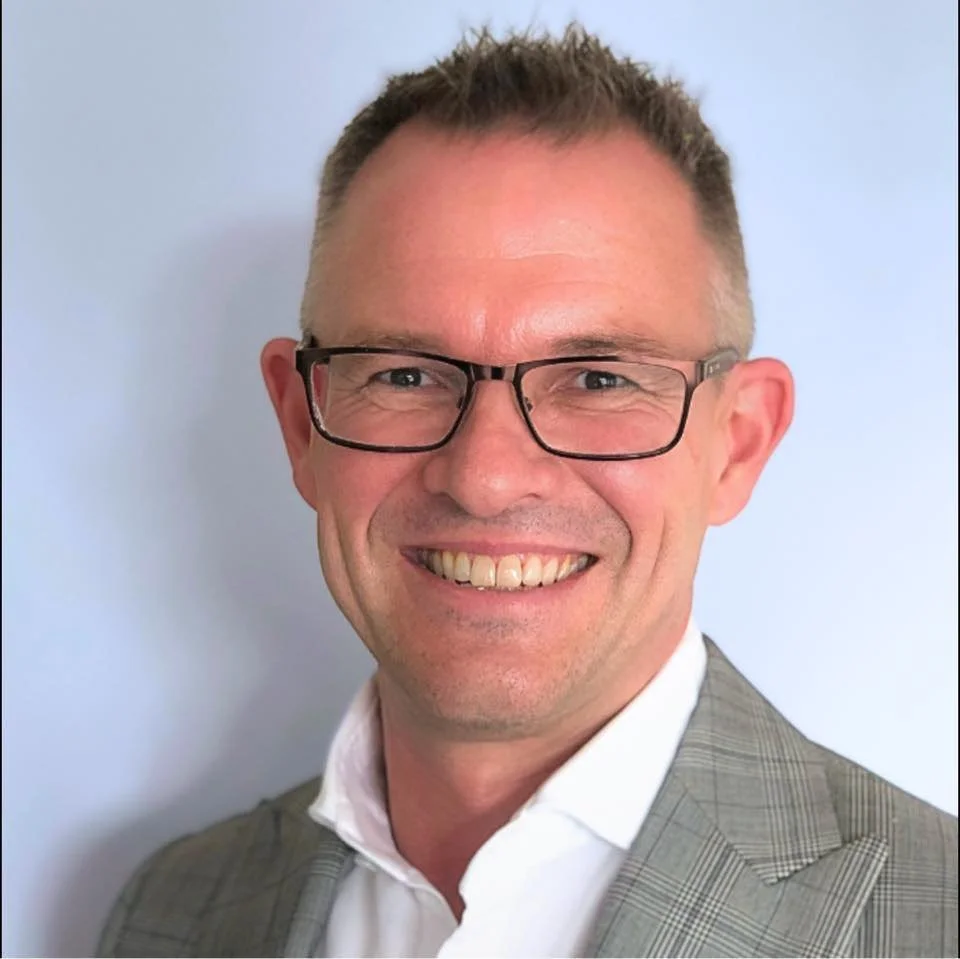 Man smiling with glasses wearing a suit, light blue background