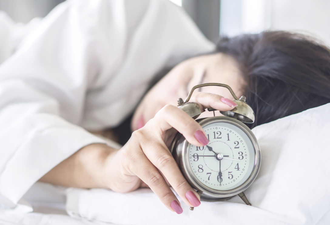 Person sleeping with hand on alarm clock fatigue