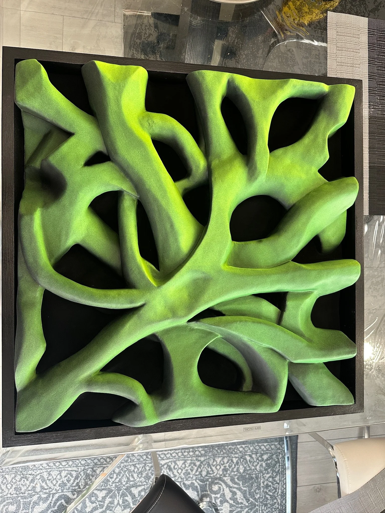 Green abstract sculpture with organic, twisting shapes in a square frame on a glass surface.