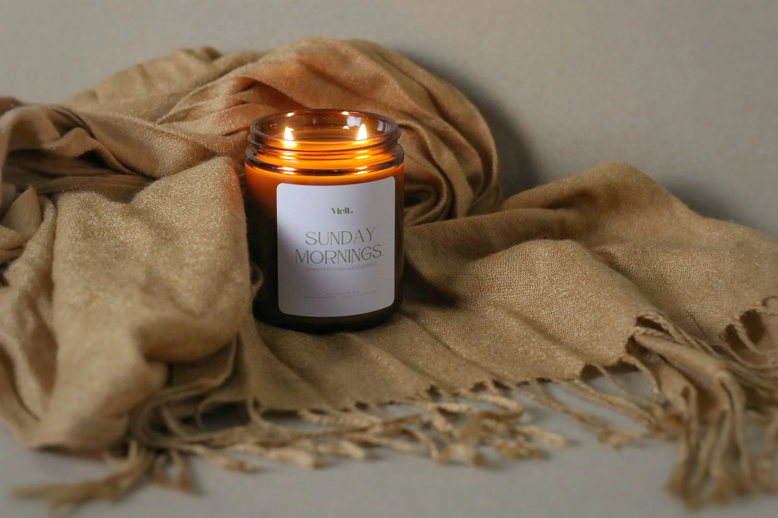 A lit candle labeled "SUNDAY MORNINGS" on a beige scarf.