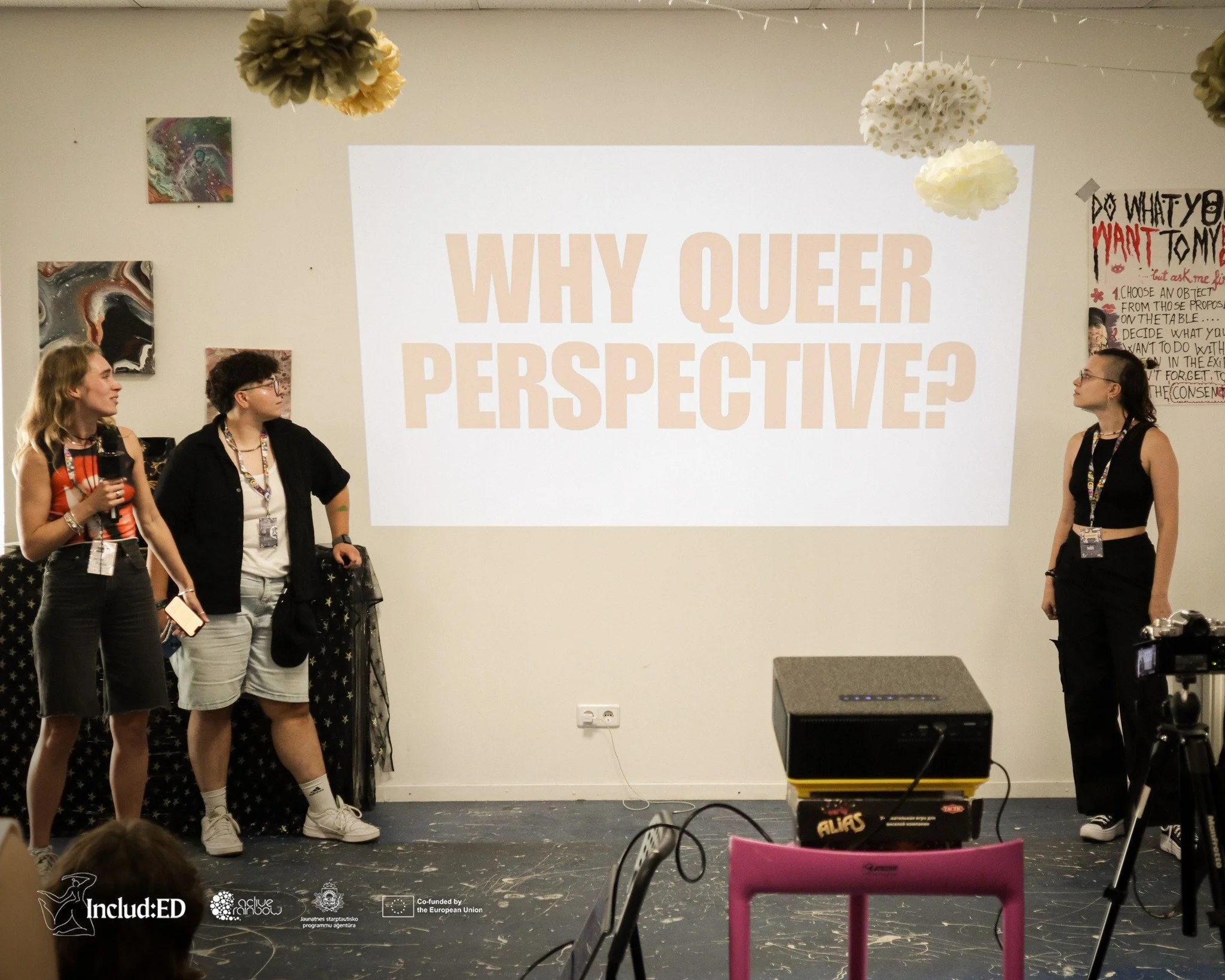 Tri osobe stoje ispred prezentacije na kojoj piše "Why queer perspective".