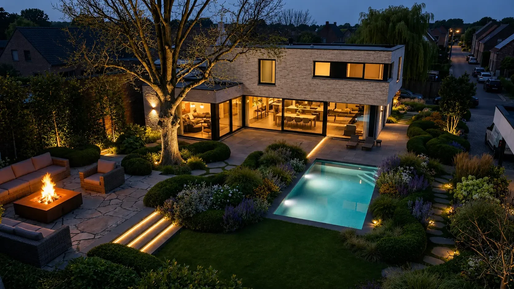 A modern house with large glass windows, outdoor patio with fire pit, swimming pool, surrounded by landscaped garden with flowers and bushes, at night with outdoor lighting.