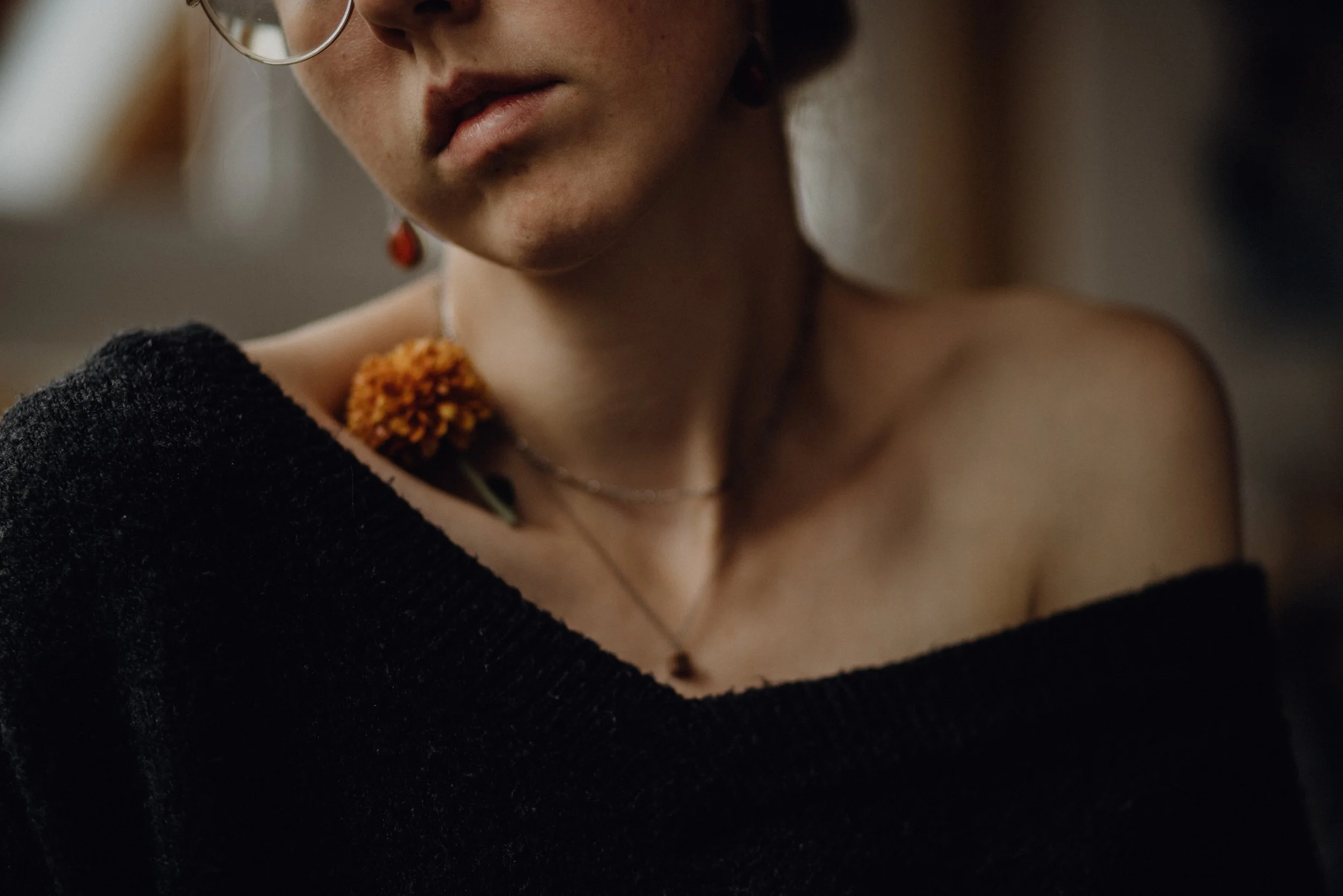 Nahaufnahme eines Schultersatzes mit einem schwarzen Pullover, Ketten und Schmuck, und einer orangefarbenen Blume auf der Schulter einer Person