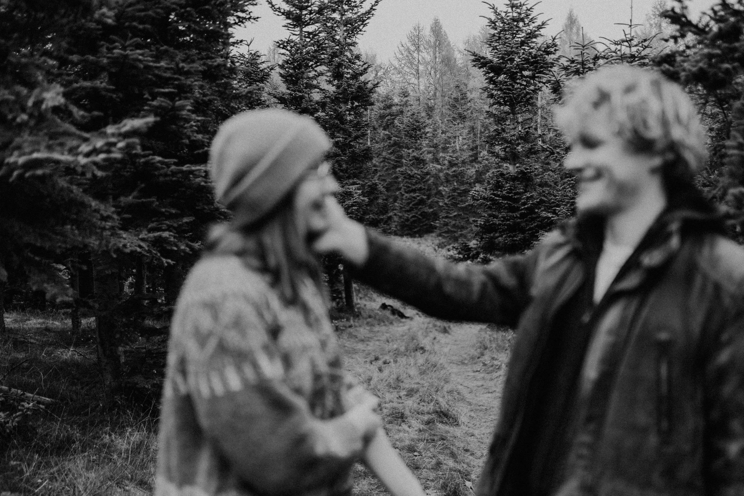 Zwei Frauen im Wald, eine gibt die Hand der anderen, beide tragen Jacken und Hüte.