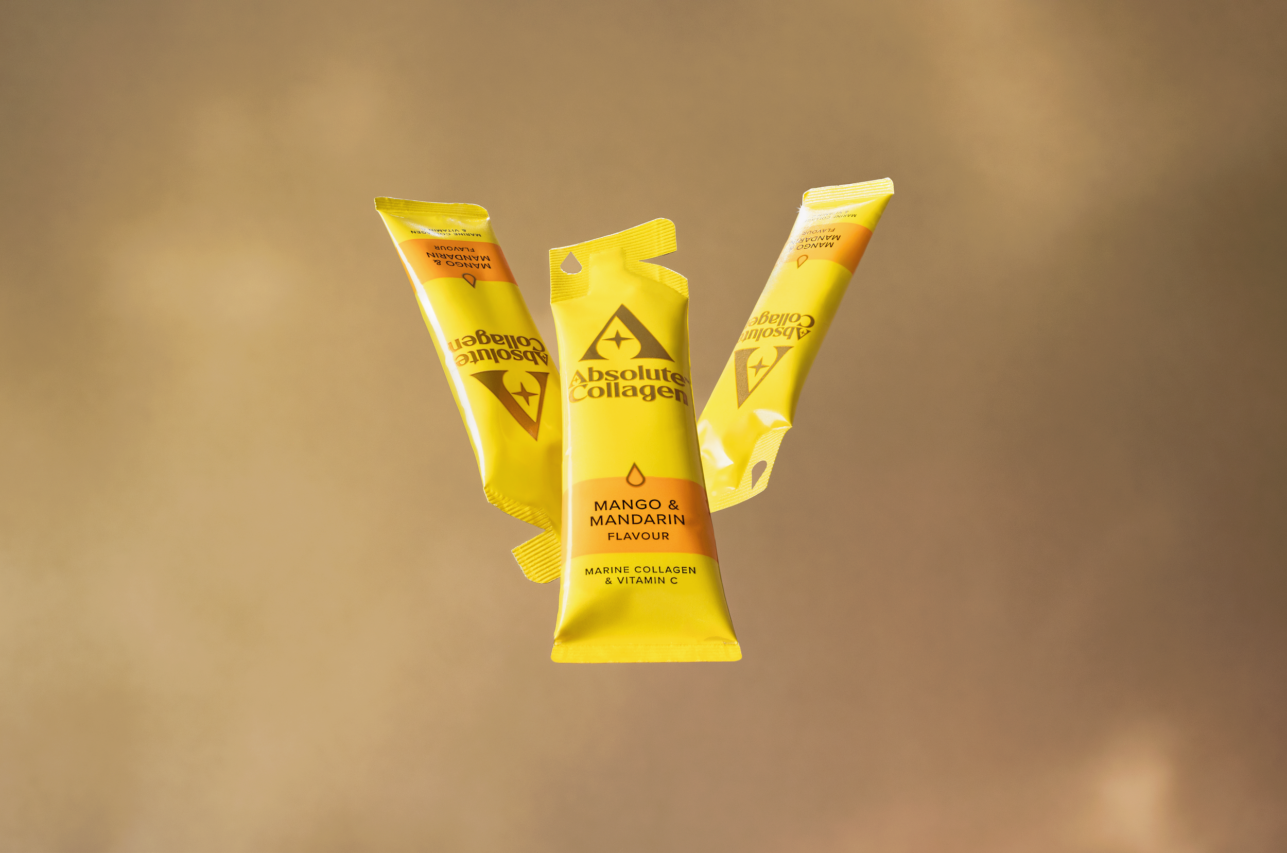 Three yellow squeeze packets of Absolute Collagen in mango and mandarin flavor floating against a gold background.