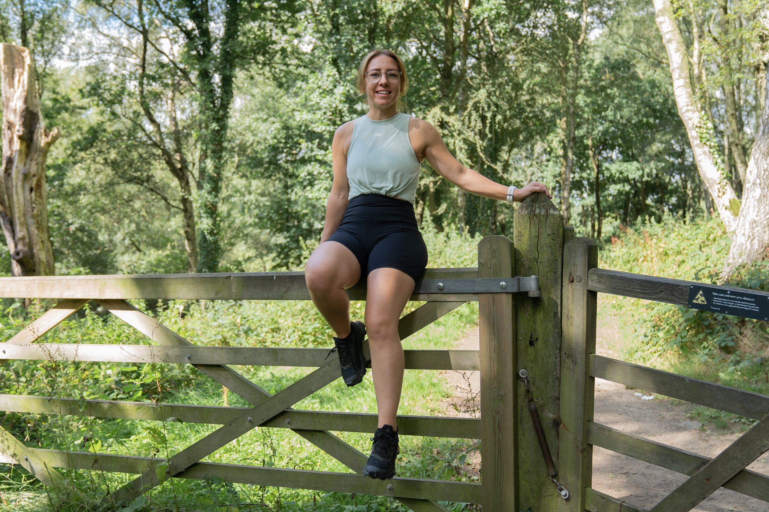 female say on a wooden fence with a green woodland behind her