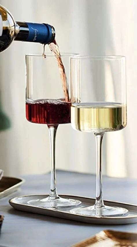 A bottle pouring red wine into a glass on a tray, with another glass of white wine beside it.