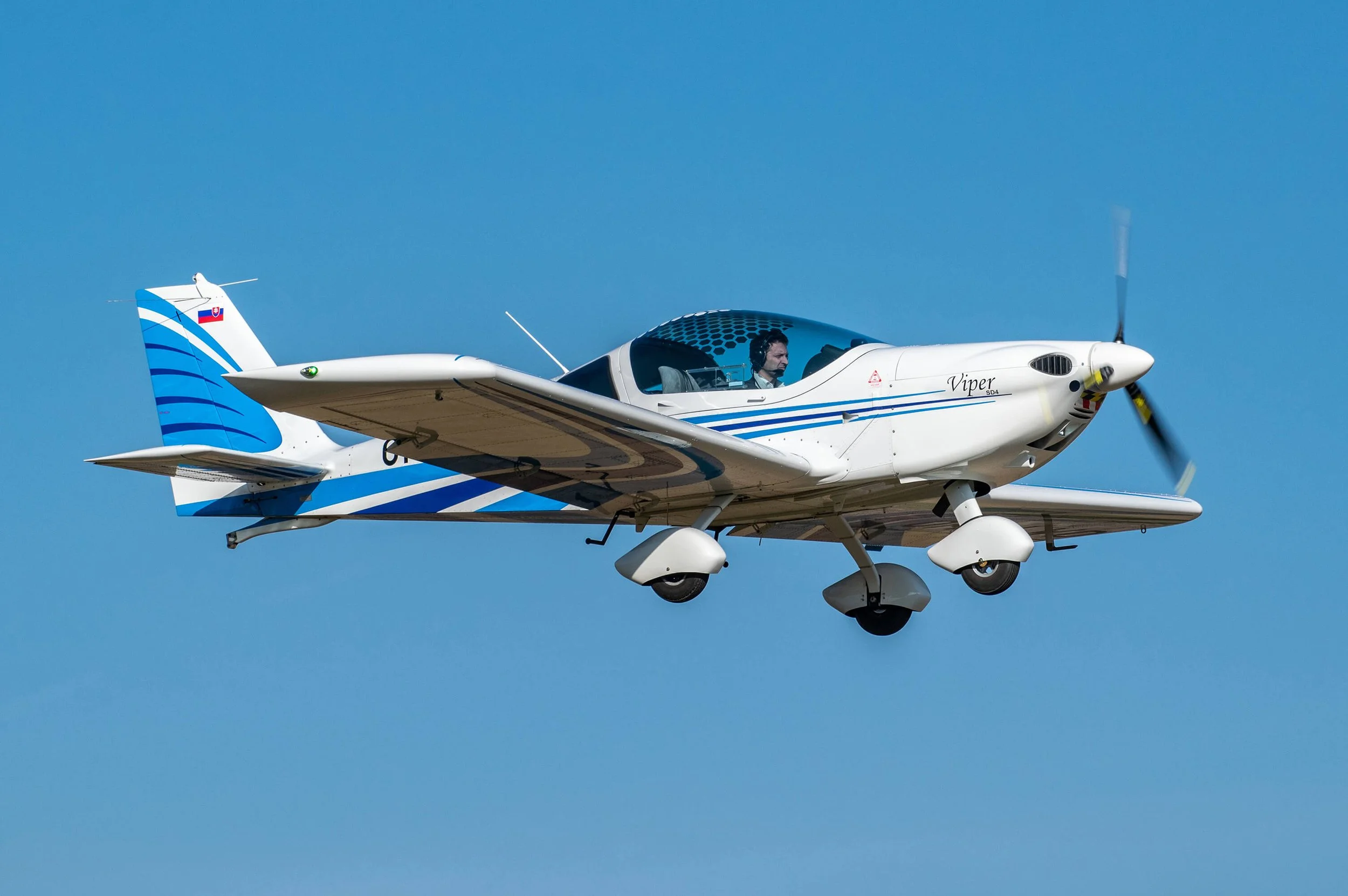 Kleine weiße Sportflugzeug mit blauen Linien fliegt am blauen Himmel.