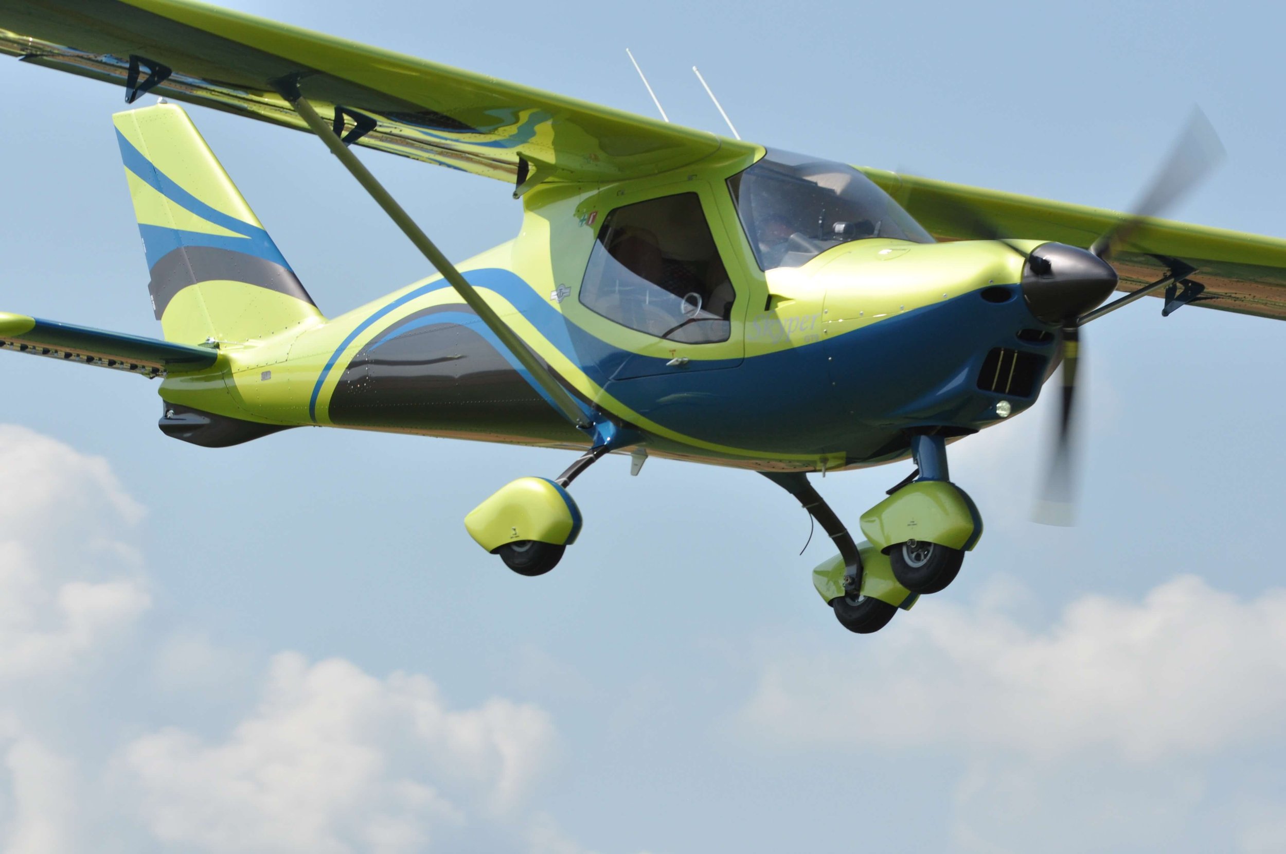 Ein gelb-blaues motorisiertes Flugzeug fliegt am Himmel.