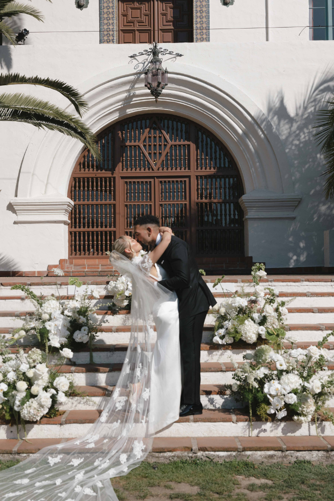 newly married couple kissing on steps surrounded by flowers in santa barbara destination wedding