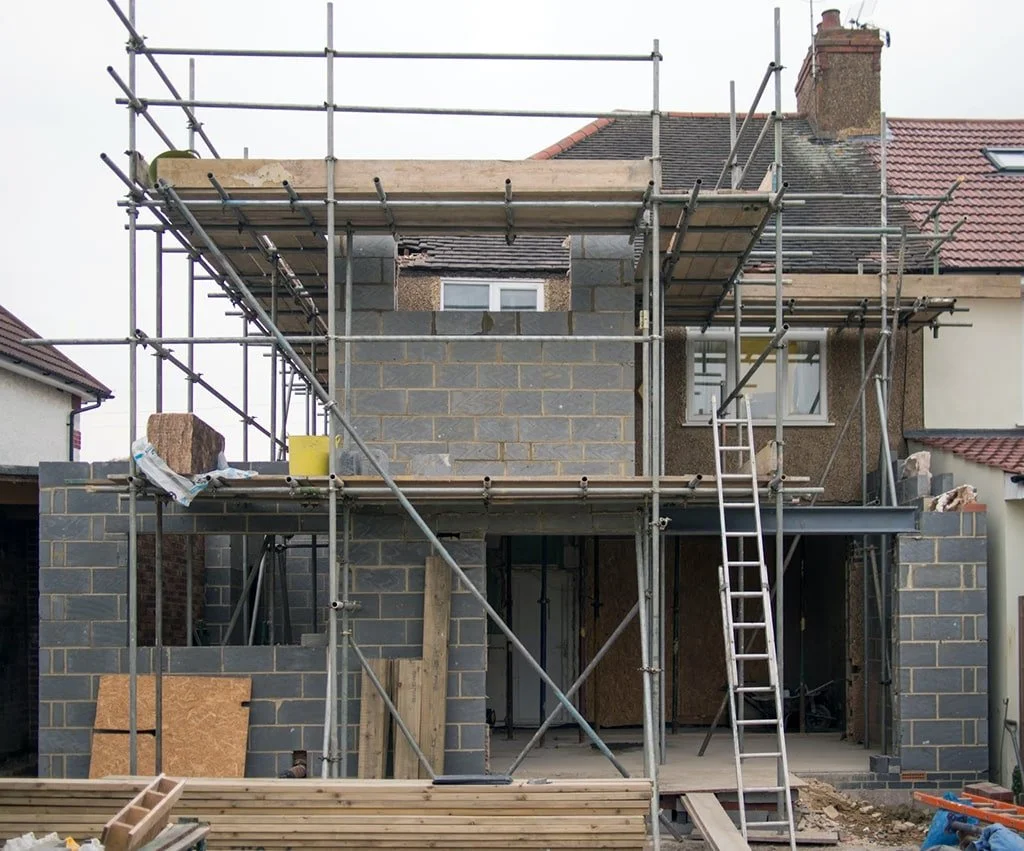 Construction site of a house with scaffolding and partially built brick walls.