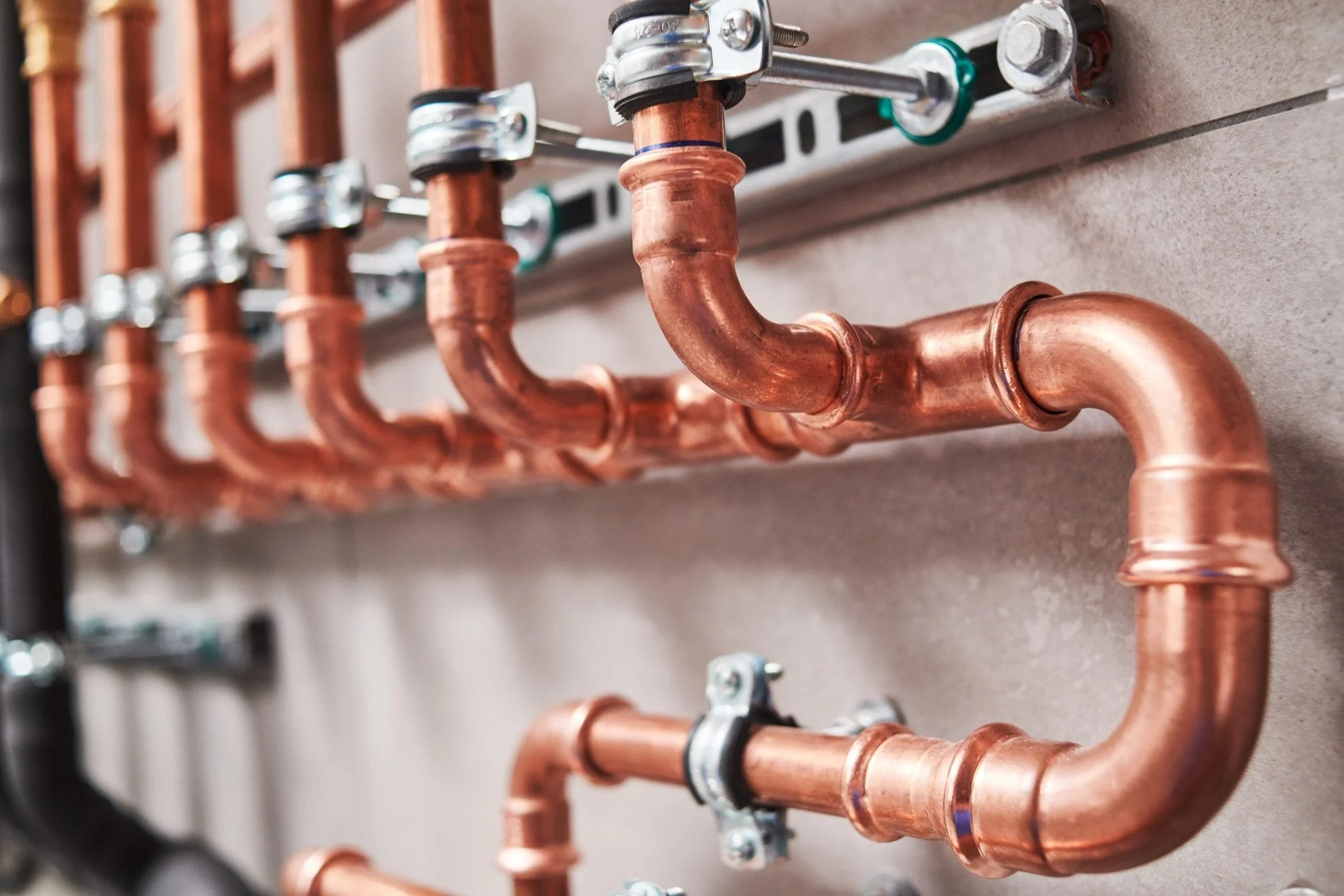 Close-up of copper plumbing pipes connected with fittings and brackets mounted on a wall.