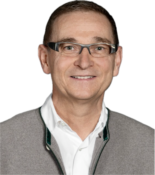 Ein Mann mit Brille, im weißen Hemd und grauer Jacke, lächelnd.