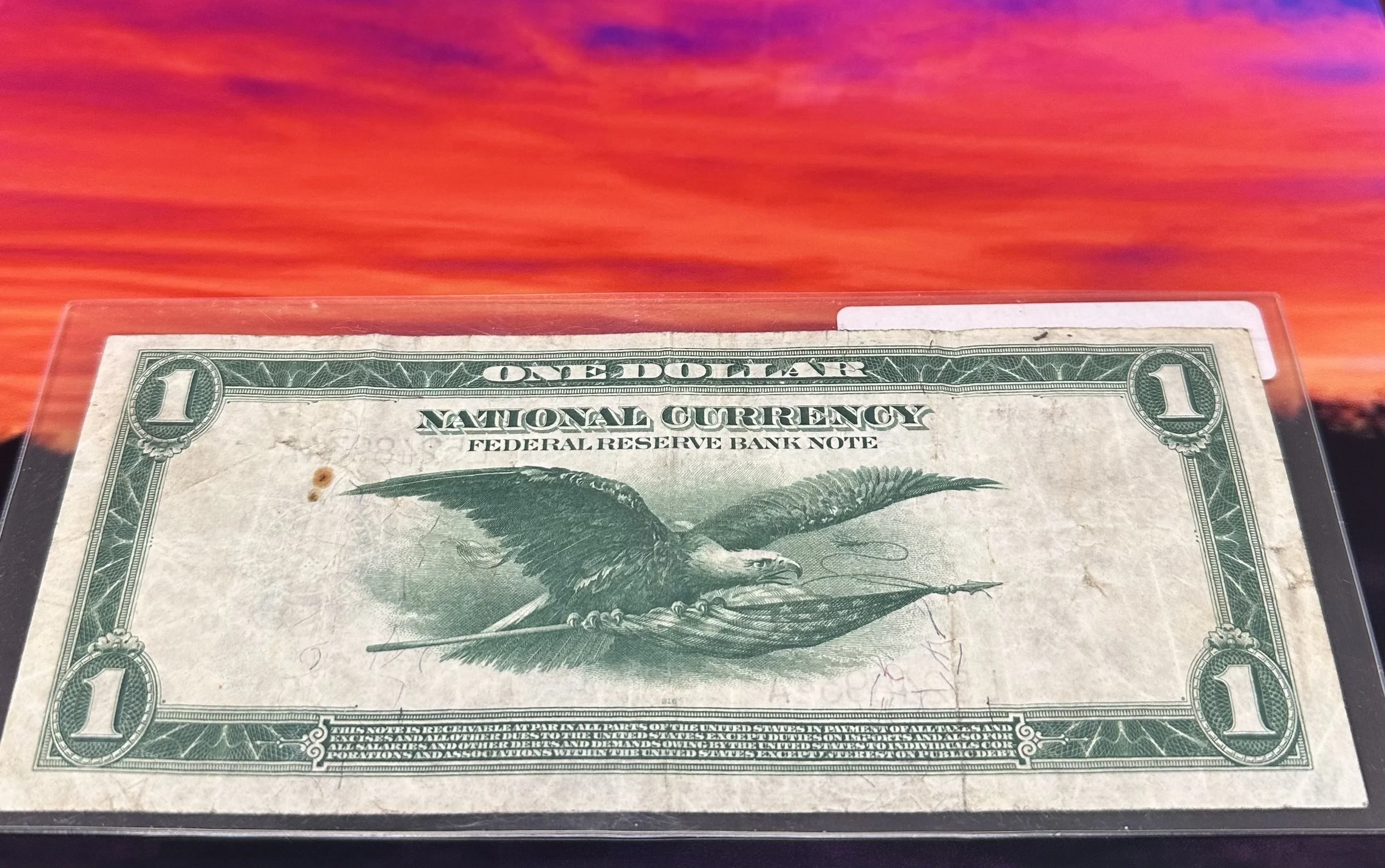 A one-dollar bill featuring an eagle with outstretched wings on a colorful sky background.