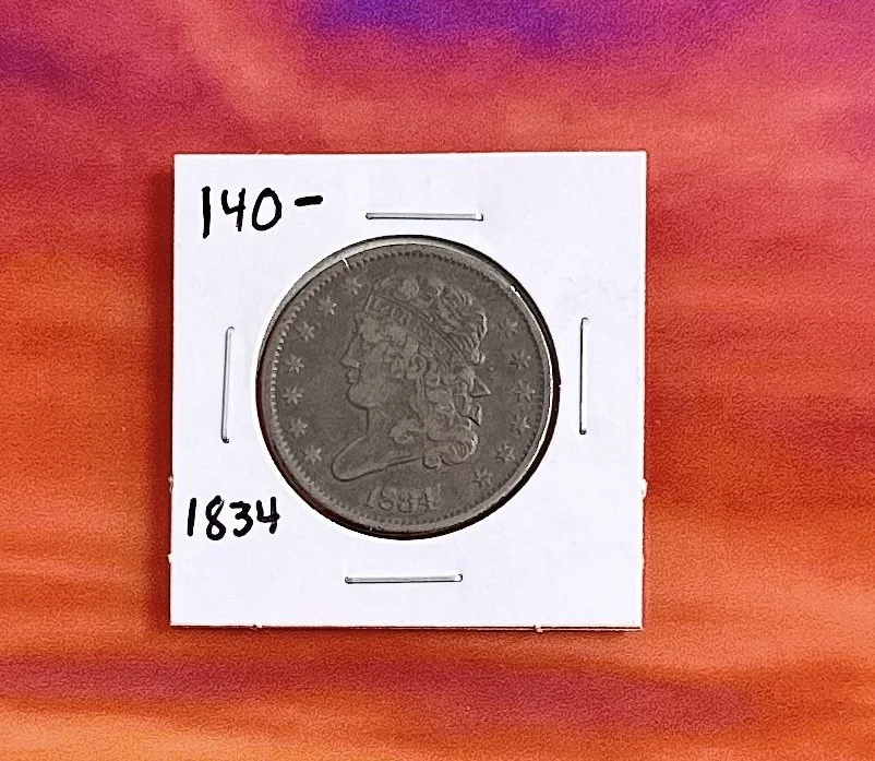 An 1834 U.S. liberty head large cent coin in a white protective holder, with handwritten numbers 140- and 1834 on the holder.