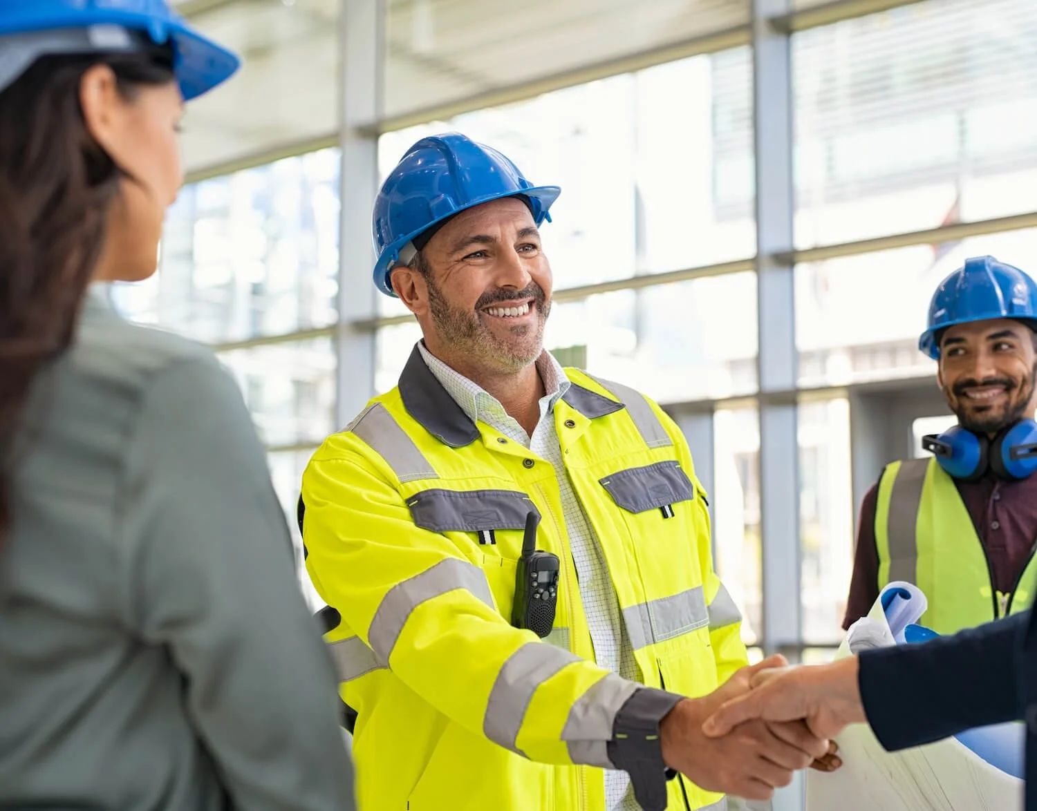 Construction workers in safety gear shaking hands inside a modern building with large glass windows.