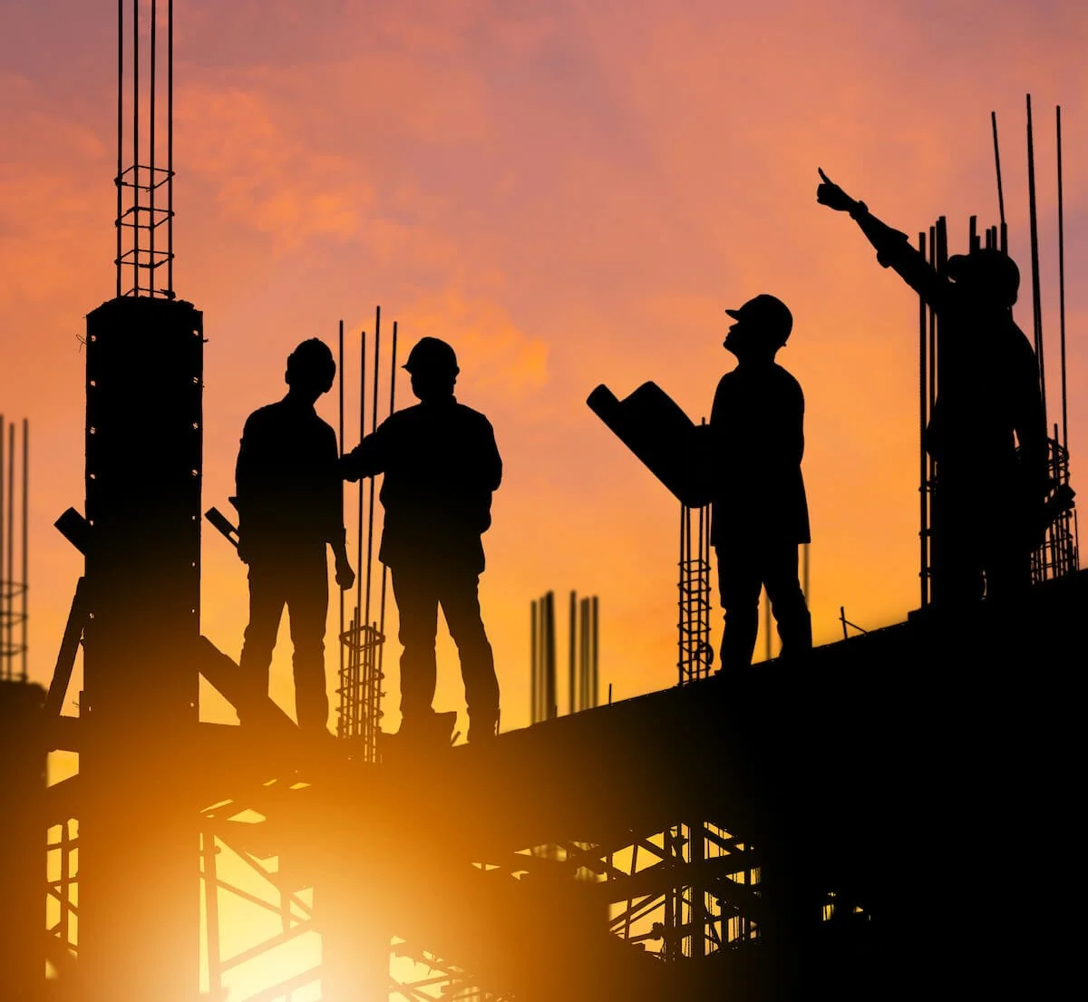silhouette of four people in hard hats on top of a building under construction at sunset