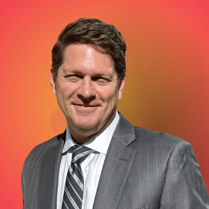 John  Buergler in a gray suit with a striped tie, smiling against an orange background.