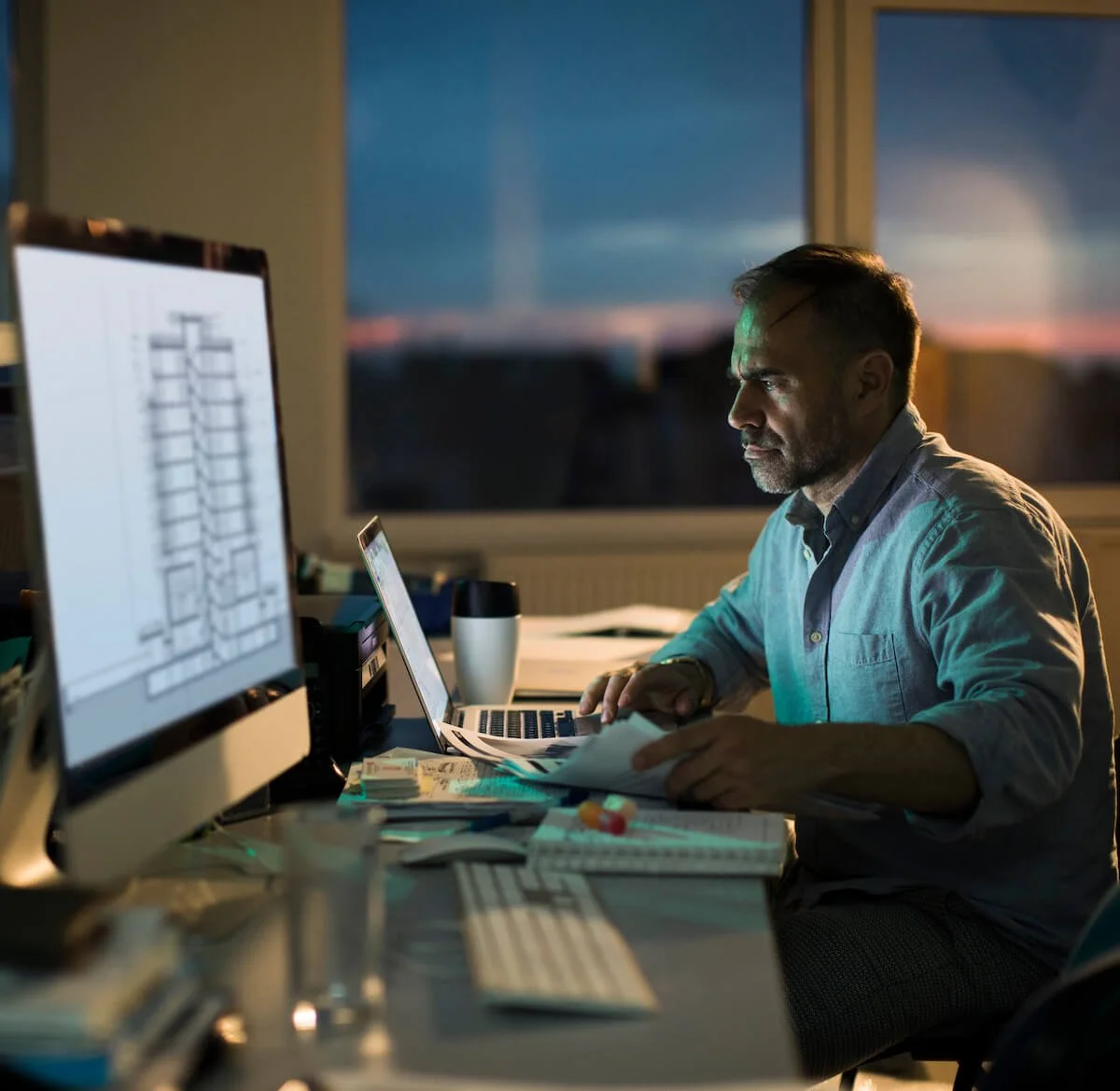 Middle aged male architect going over building plans while working overtime at night in his office