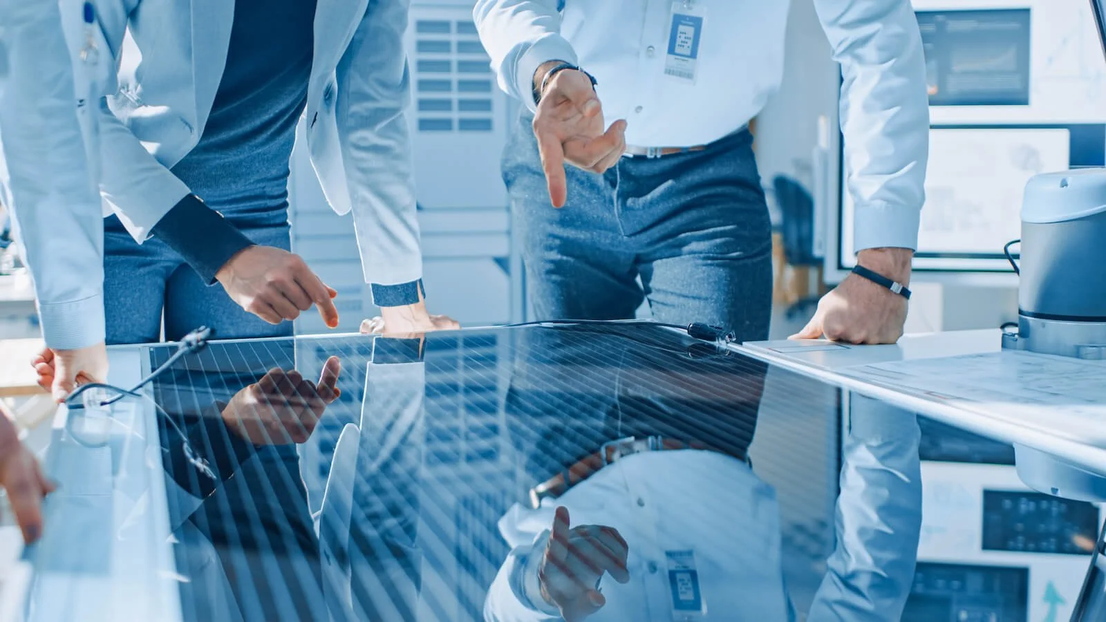 Scientists in lab coats examining a large solar panel in a laboratory setting.