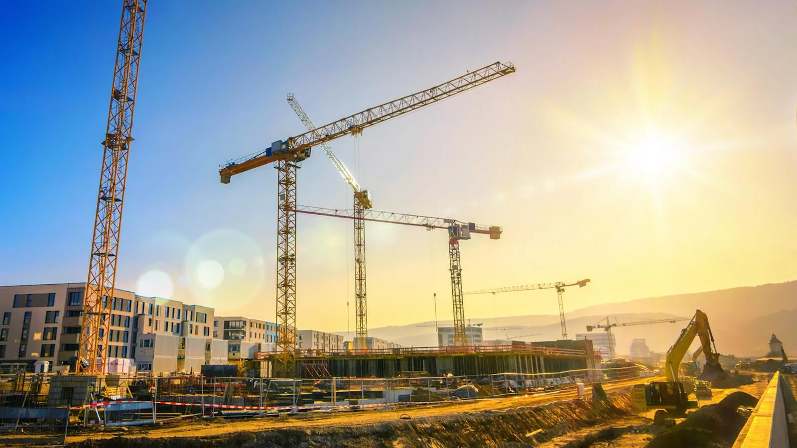 Construction site with multiple yellow cranes, building structures, and construction vehicles, under a bright sun in the sky.