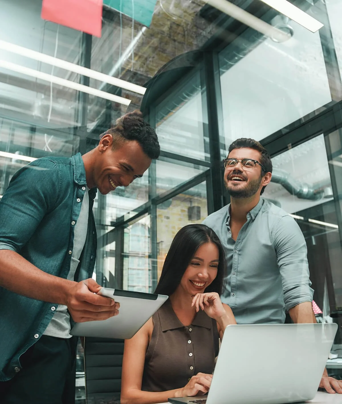 Group of three young and positive employees using modern technologies and smiling while working in modern office