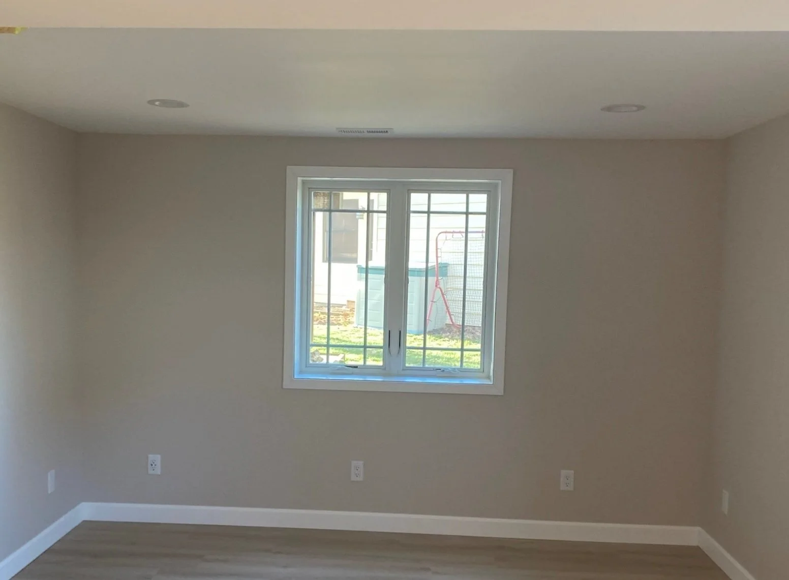 Empty room with beige walls, a window with bars, and hardwood flooring.