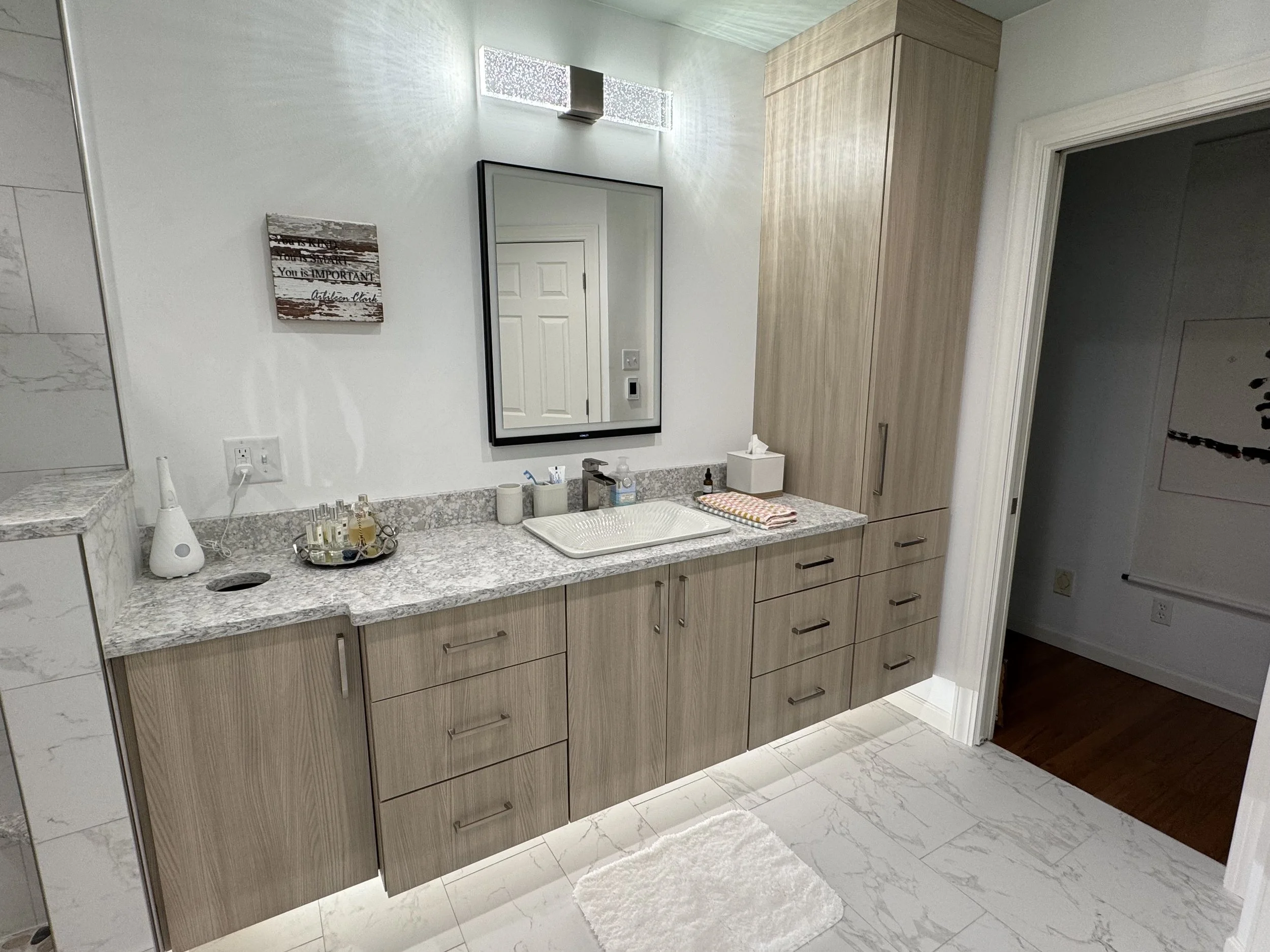 A modern bathroom vanity with a marble countertop, a rectangular sink, and a mirror, with various toiletries and a tissue box on the counter.