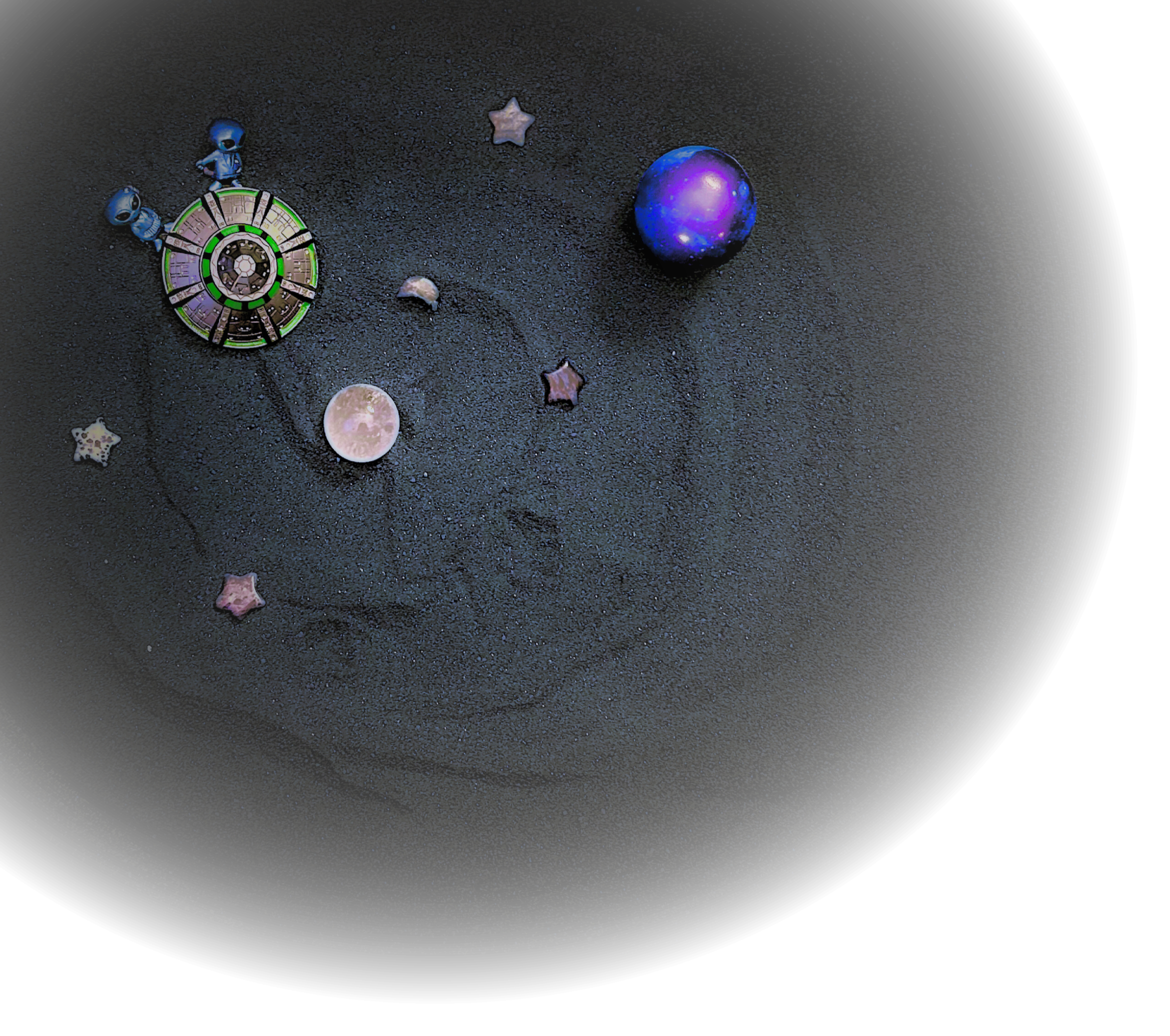 An image of a sandtray scene made in black sand depicting two aliens riding a spaceship among stars and planets.