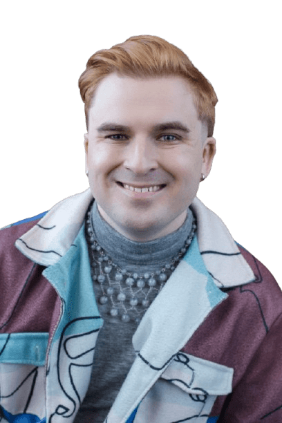 A picture of the therapist, Elijah Eiler, LCSW. They are smiling and looking into the camera. They are wearing earrings, a necklace, and a multi-colored jacket.