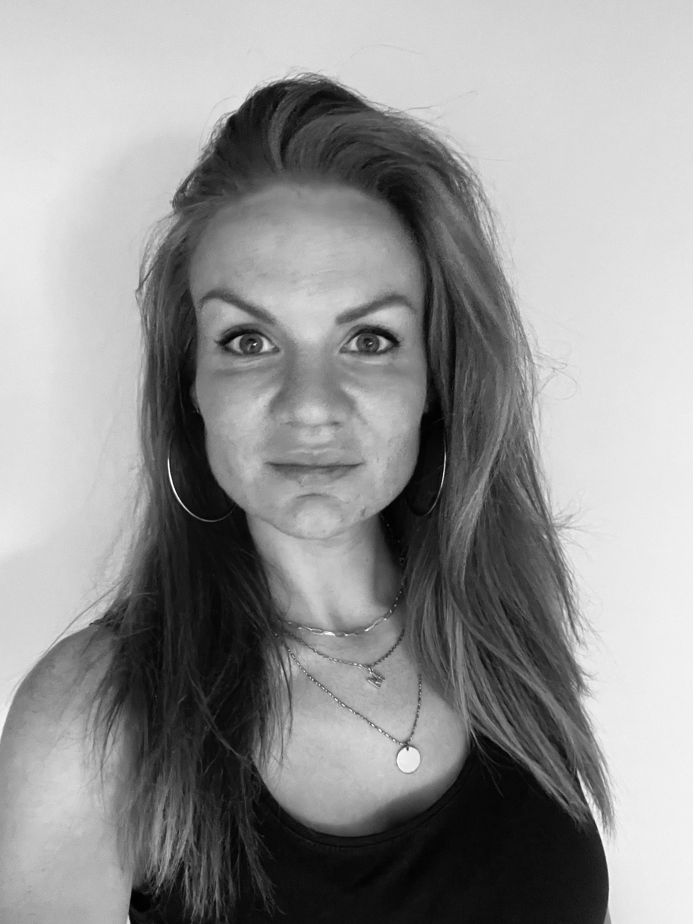 A woman with red hair, wearing a yellow off-shoulder top and large earrings, sitting at a restaurant table with a dish of food in front of her. The background shows other diners and a city street view.