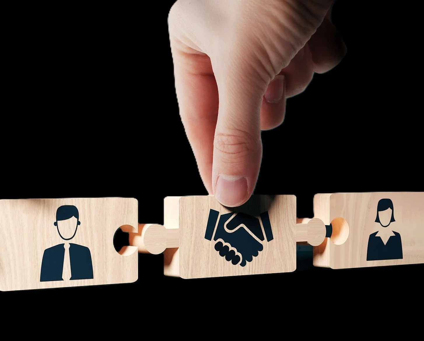 A hand placing a wooden puzzle piece with a handshake icon between two icons of a man and a woman against a black background.