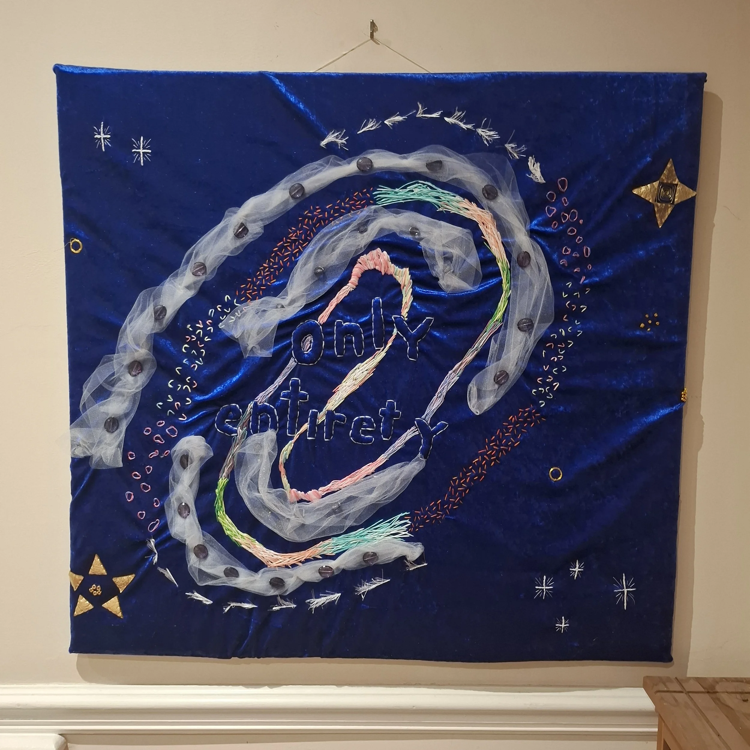 a multicoloured embroidery design on ultramarine blue velvet. the central design reads "only entirety"
