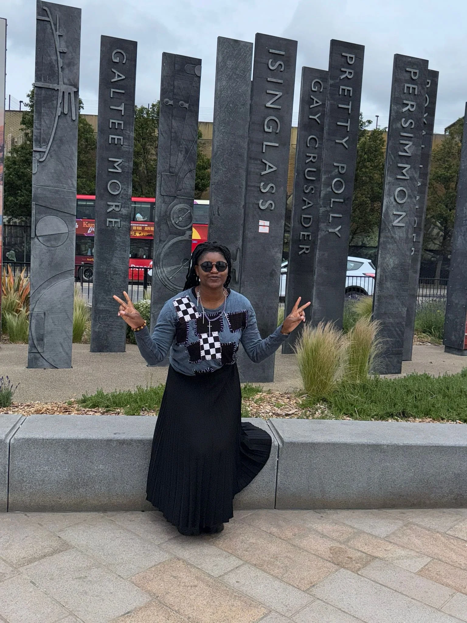 A woman with long, braided hair, wearing a blue pullover with black and  white patches,  and a long flowing black skirt