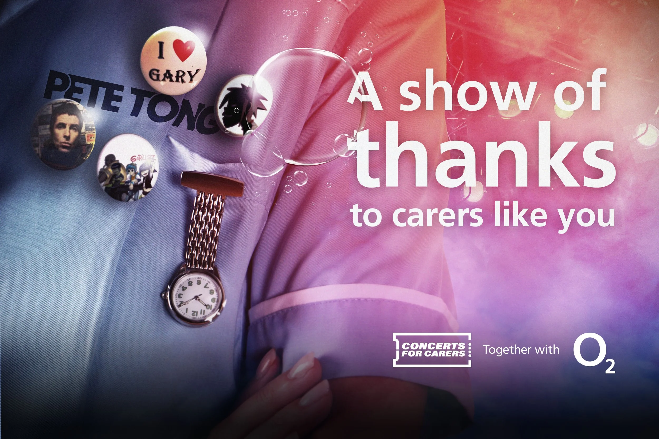 A person holding a pink booklet with bubbles, pins, and badges attached to it. The badges include one with a portrait of a man, one with a cartoon character, and another with the text 'I ❤️ GARY'. The booklet has the words 'A show of thanks to carers like you' and mentions a concert with O2.