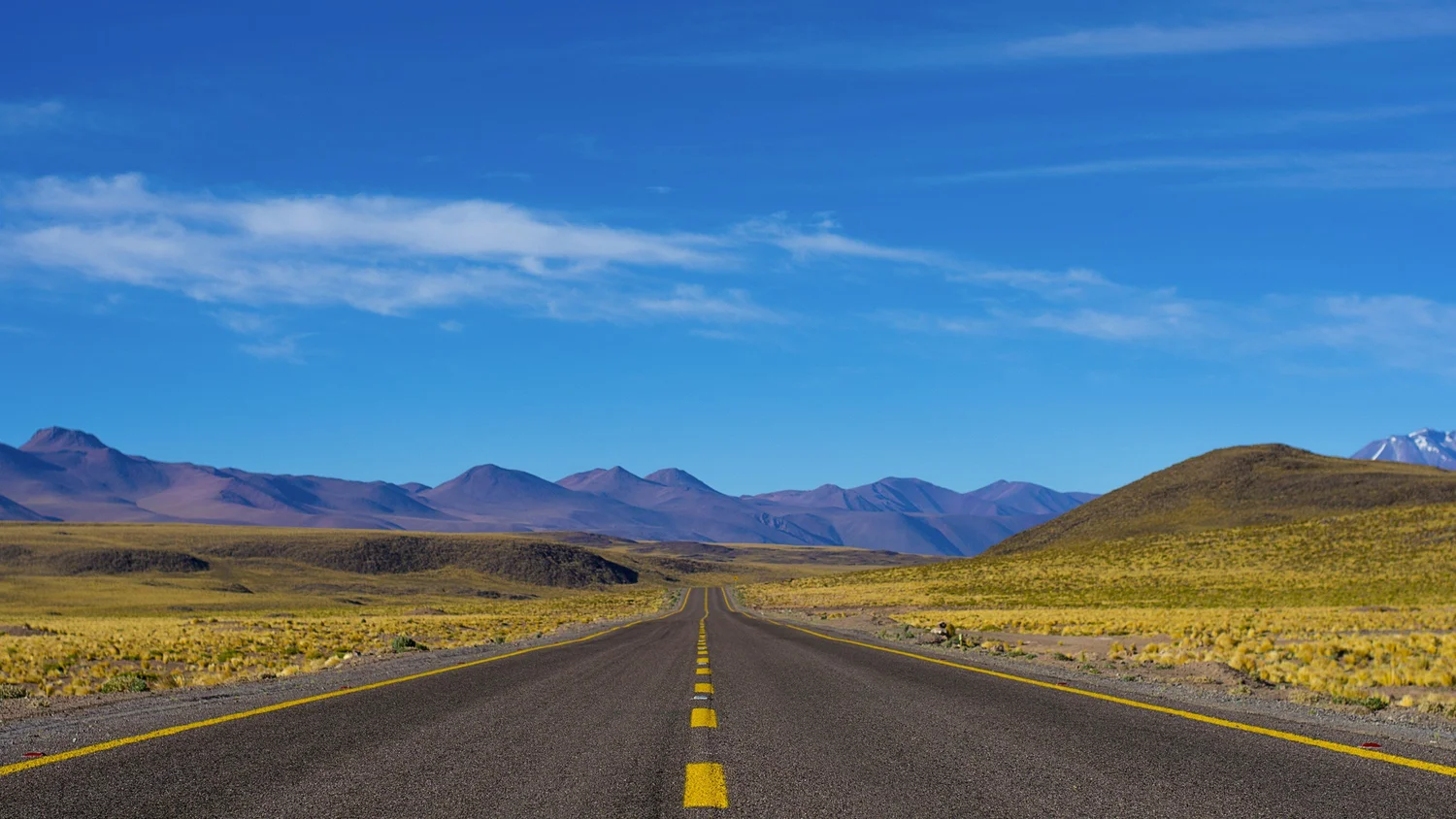 Open road stretching toward mountains under a blue sky
