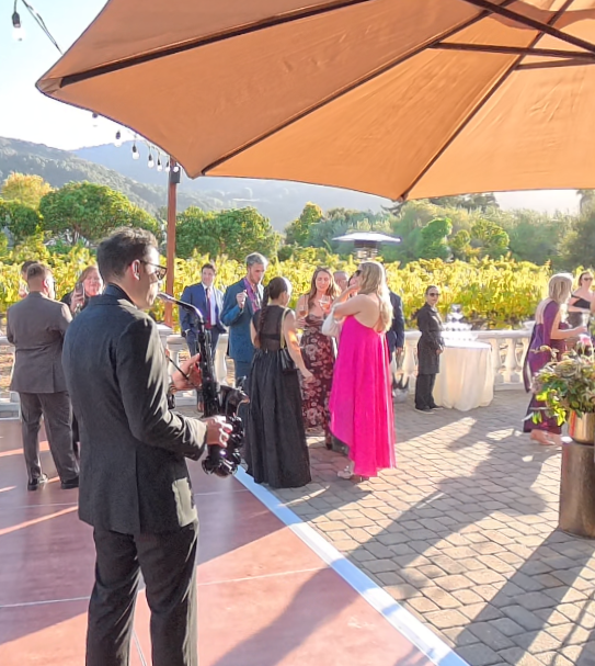 Ant Smith performing live saxophone among guests during cocktail hour at a vineyard wedding.